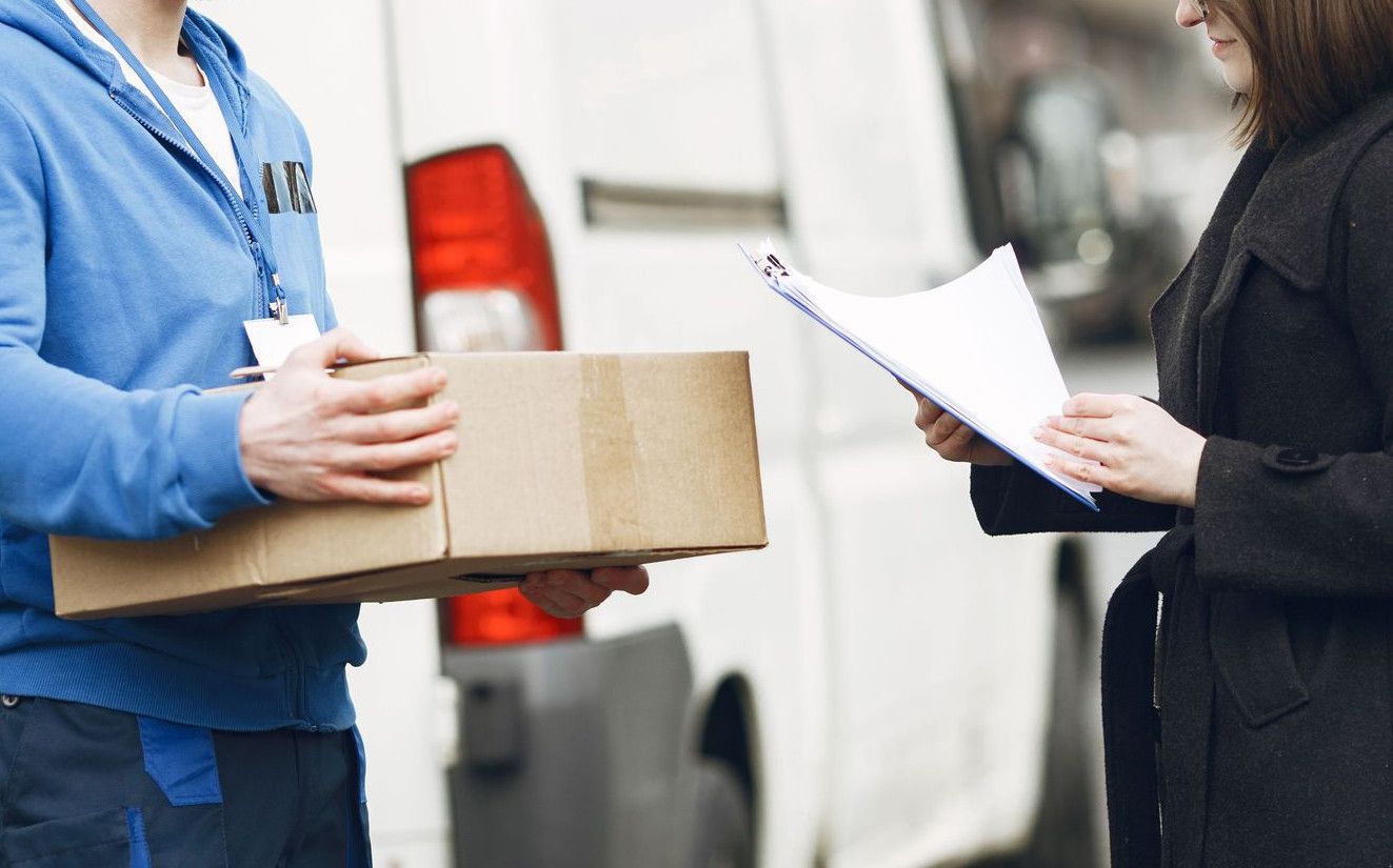A courier hands over a package to a woman client on a city street, facilitating delivery service.