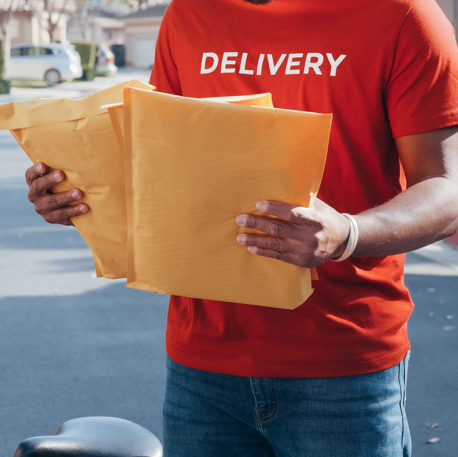 A delivery man in a red uniform holds envelopes while standing outdoors.